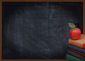 A stack of books with a red apple on top in front of an out of focus chalkboard. Back to school or education concept. Vintage effect with vignette added.